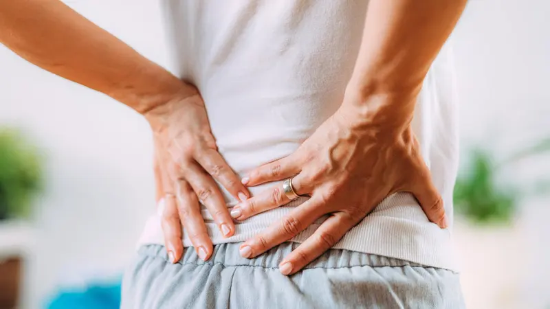 A person in a white top holds both hands against their lower back