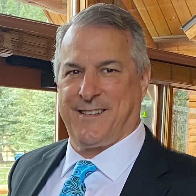 Brett Hightower: Smiling man with gray hair in a dark jacket and blue paisley tie, seated near a window
