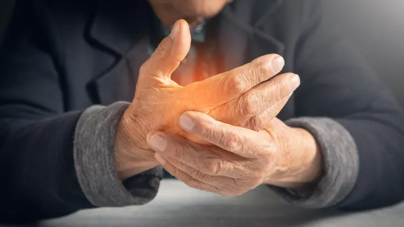 An older person holds and rubs one hand in discomfort, with a warm glow over the fingers