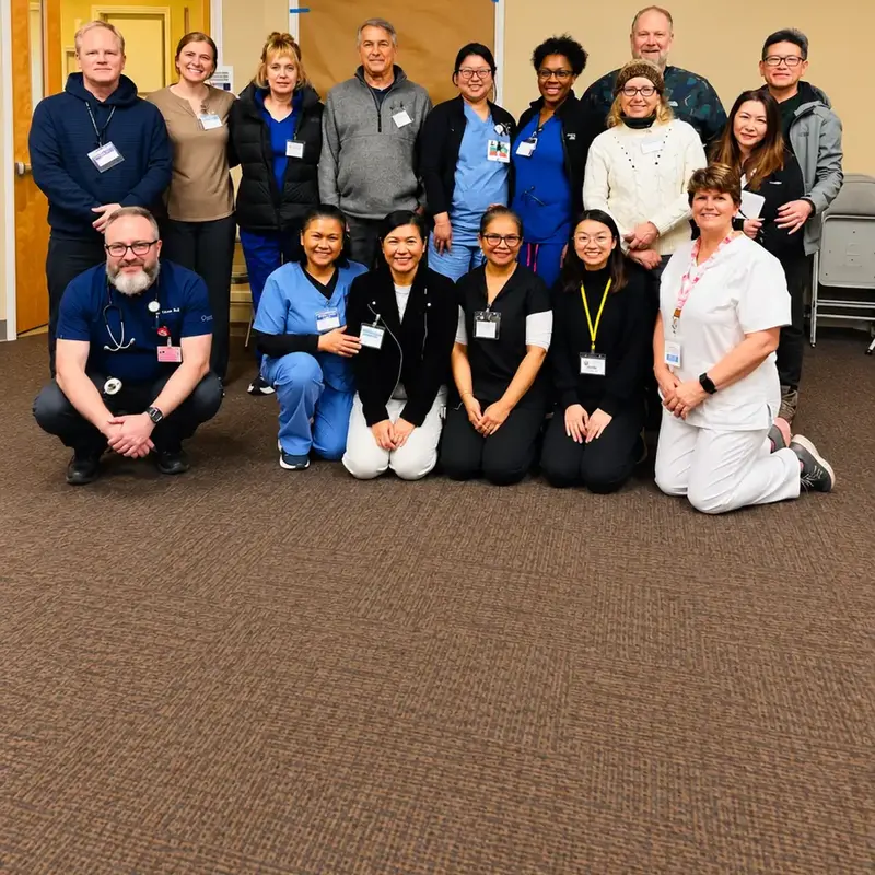 A group of about sixteen staff and visitors posing together in a carpeted room, some standing and some kneeling in front